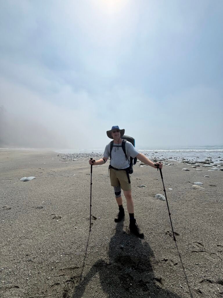 Jason Van Bergen wearing a heavy backpack and knee brace on the beach during the West Coast Trail.